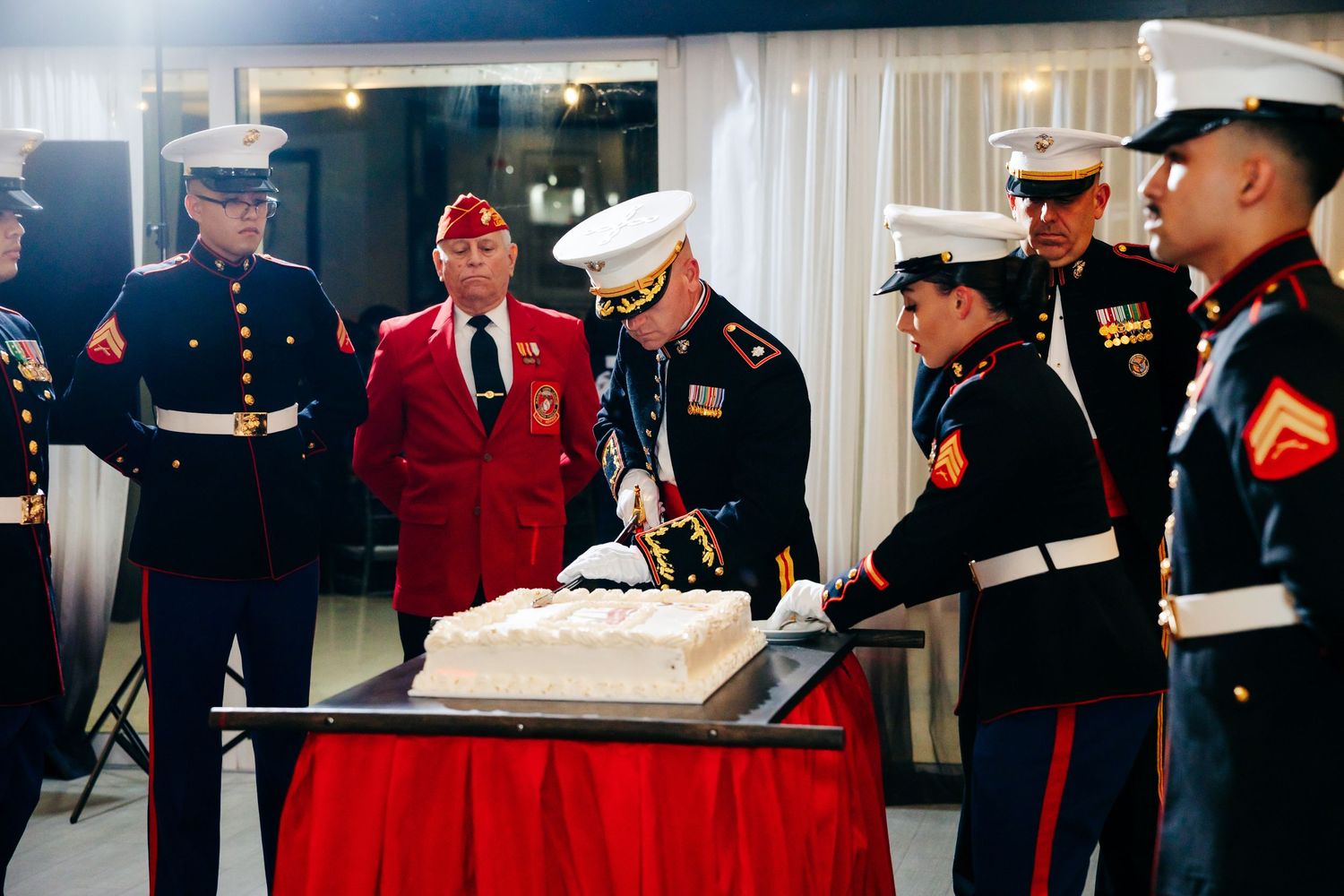 Marines in dress uniforms participate in a ceremonial cake cutting at a formal event.
