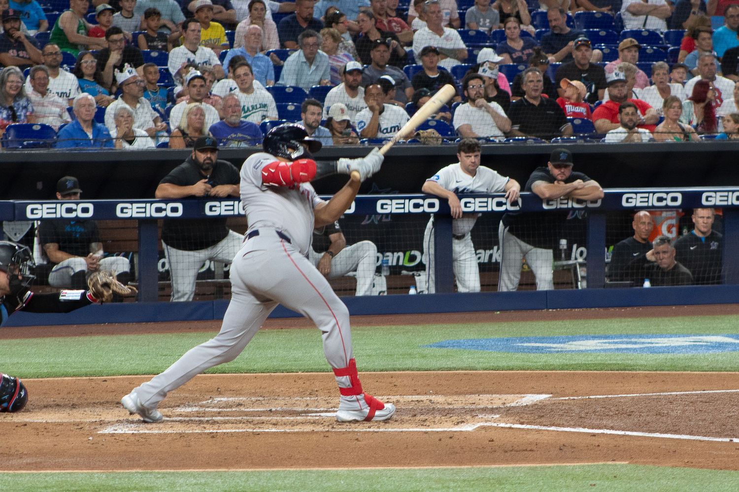 Baseball batter in red and white uniform swings at pitch during game.