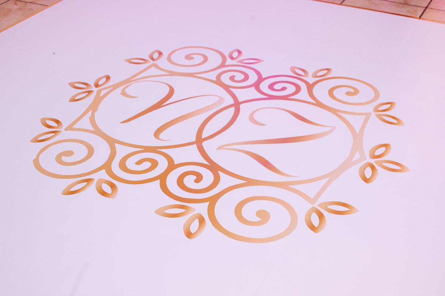 Elegant monogram design in rose gold color with swirling decorative elements on white background.