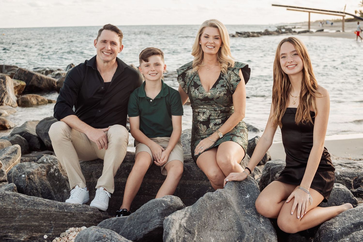 Family poses on rocky shoreline with ocean and sunset in background.