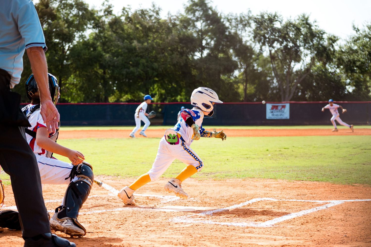 Baseball player slides into home plate during a game on a sunny day at a baseball field.