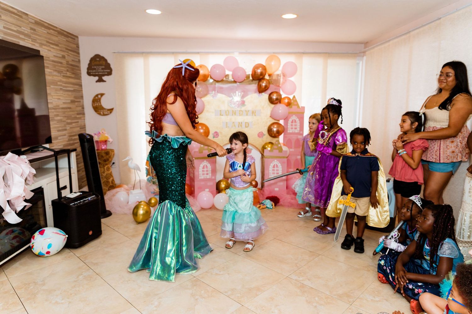 Children and guests gathered in a room decorated for a princess-themed party celebration.