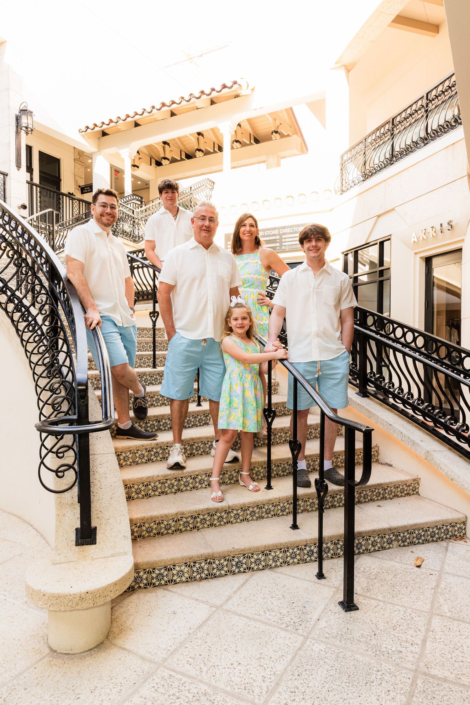 A family poses together on an elegant staircase with ornate iron railings and Spanish-style tile accents.