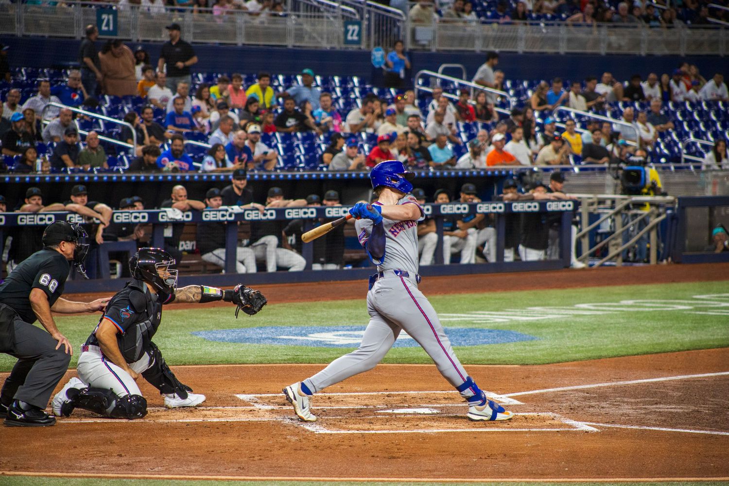 Baseball batter swings at pitch during professional game with crowd in blue stadium seats behind home plate.