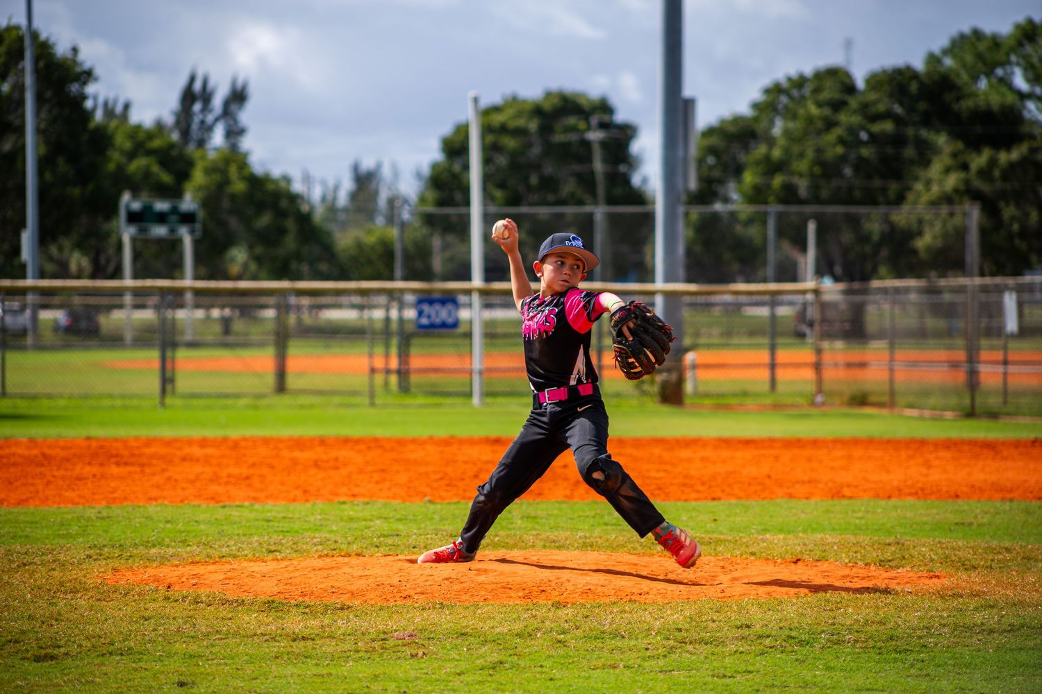 A baseball player in a red uniform delivers a pitch on a sunny day at a baseball field.