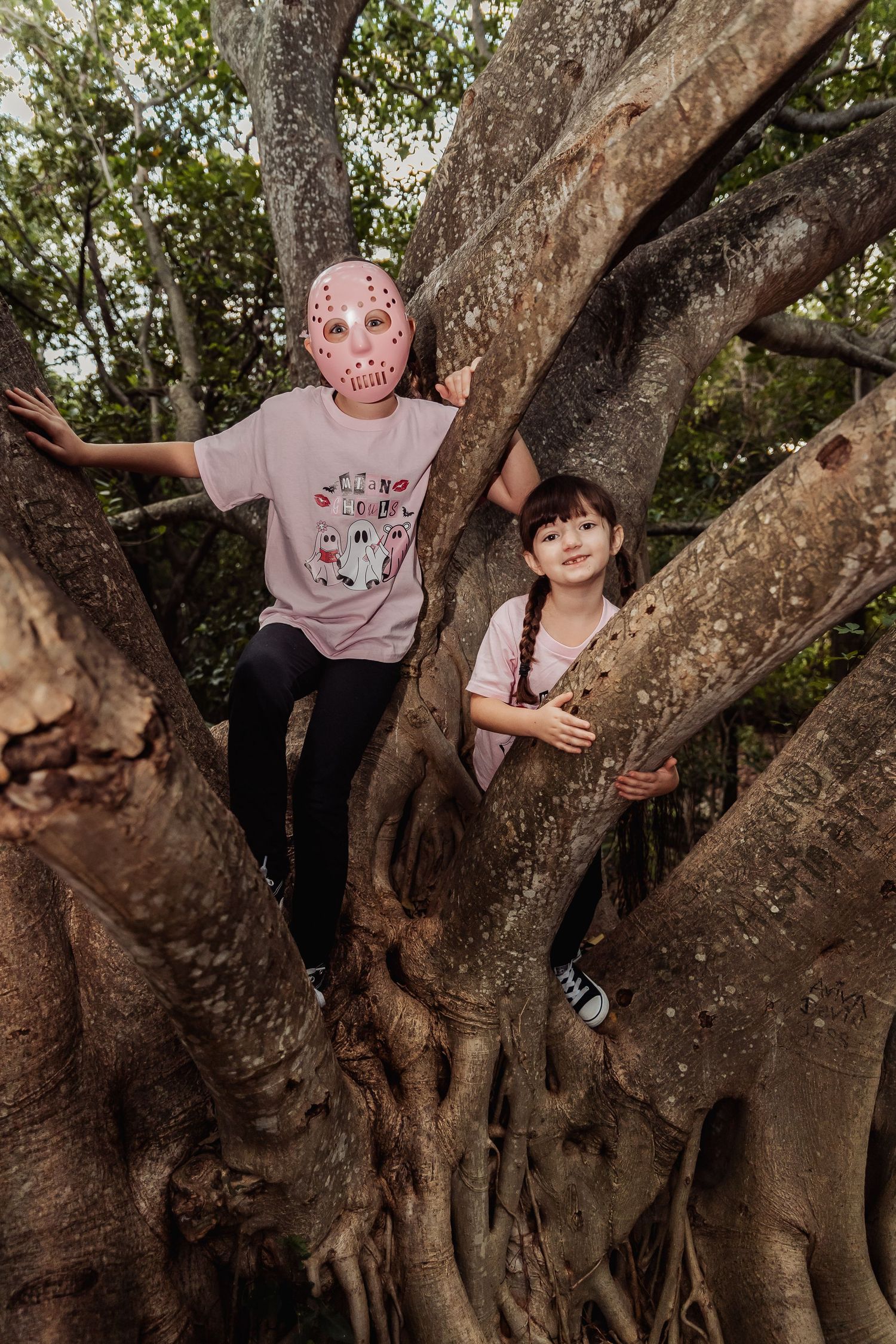 Children climb and play on a large gnarled tree trunk with exposed roots in a natural outdoor setting.