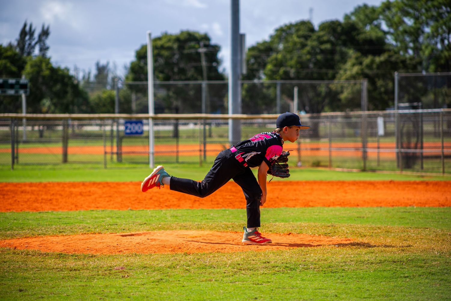 Baseball player in pink uniform diving to make a dramatic catch on a sunny day at a baseball field.