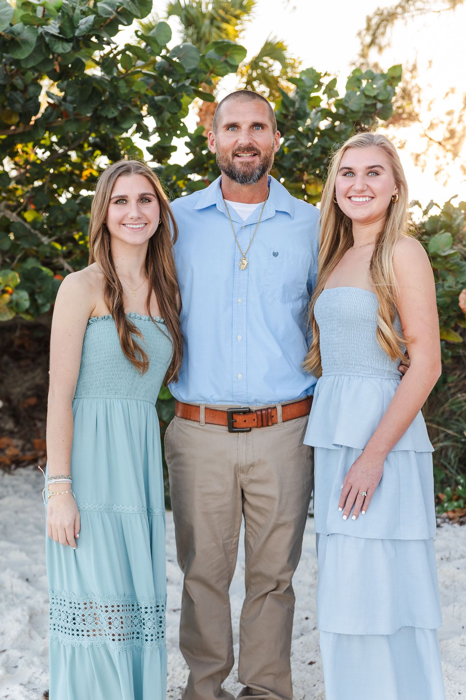 Three people in coordinating blue and khaki outfits pose together for a casual outdoor portrait.