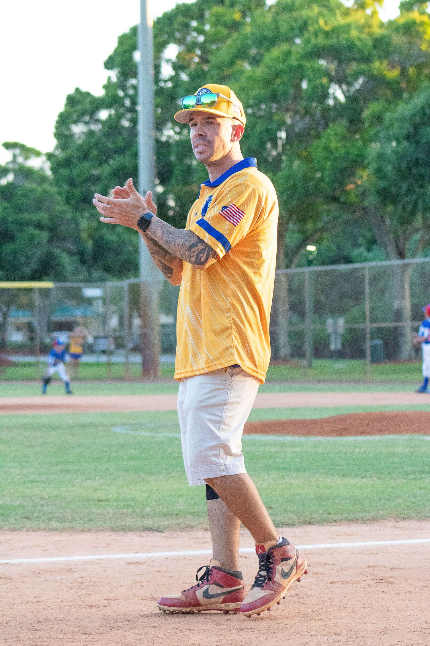 Coach in yellow jersey and cap stands on baseball field giving instructions.
