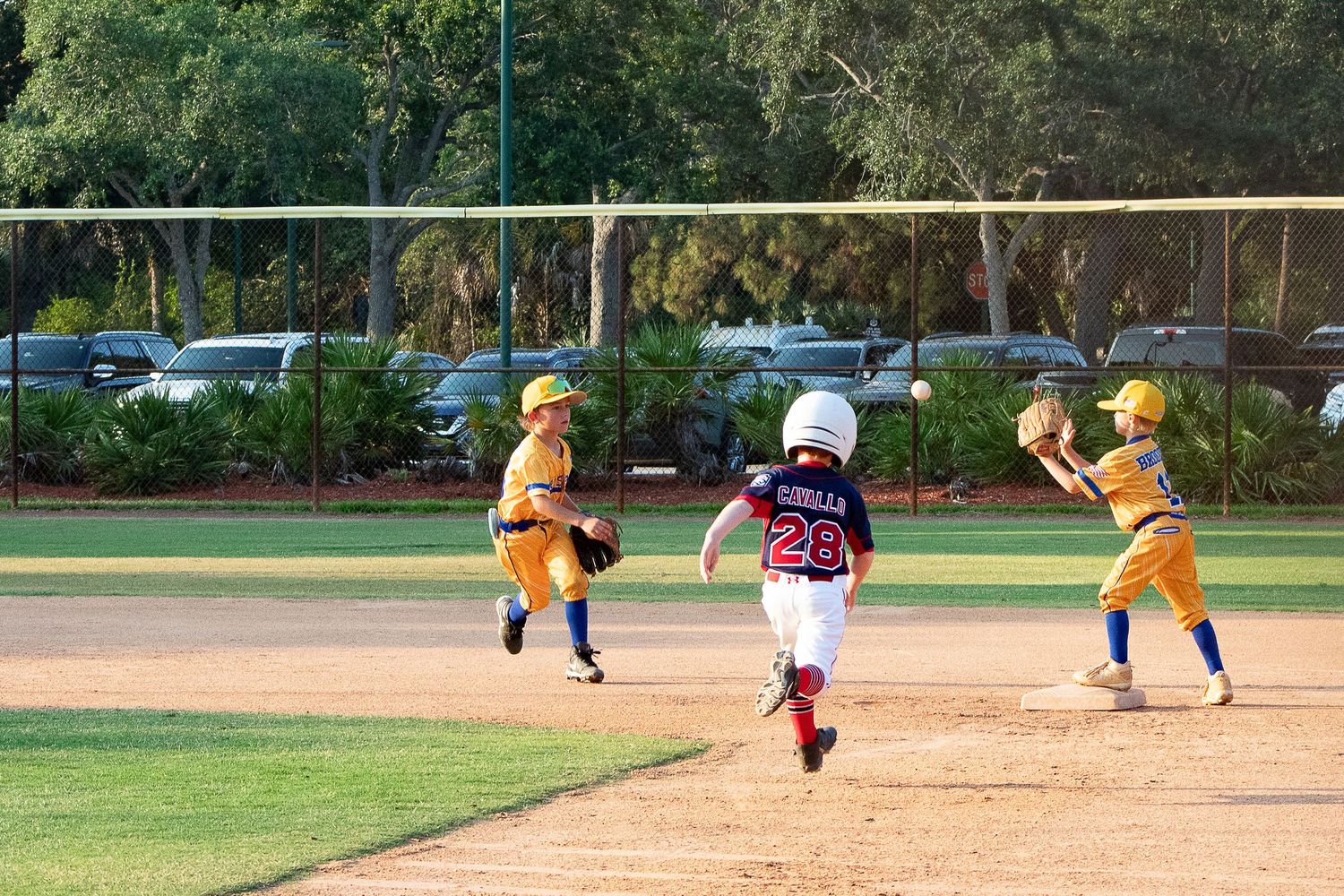 Baseball players running between bases during a youth league game on a sunny day.