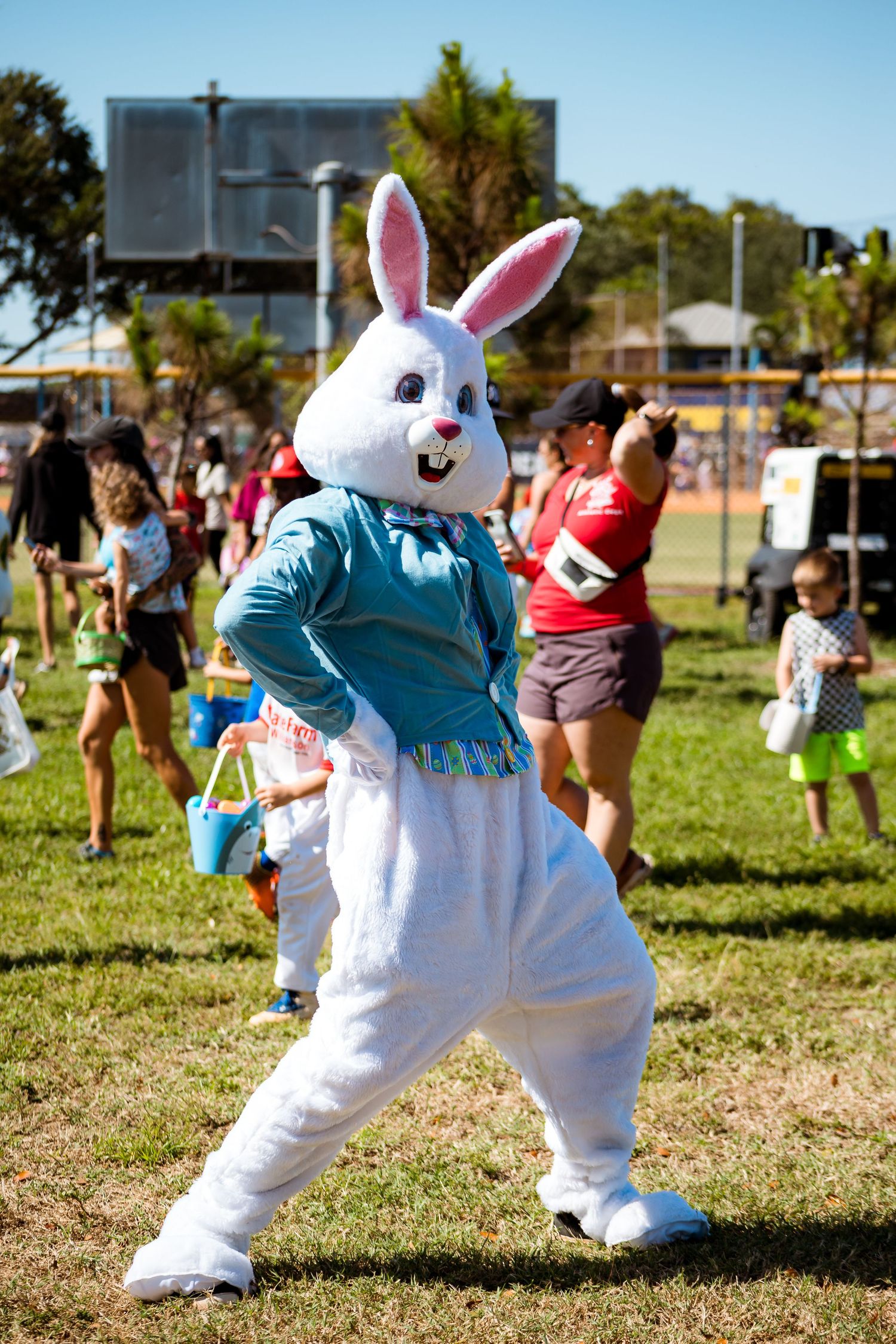 Easter Bunny mascot in white costume and blue vest poses energetically at outdoor community event.