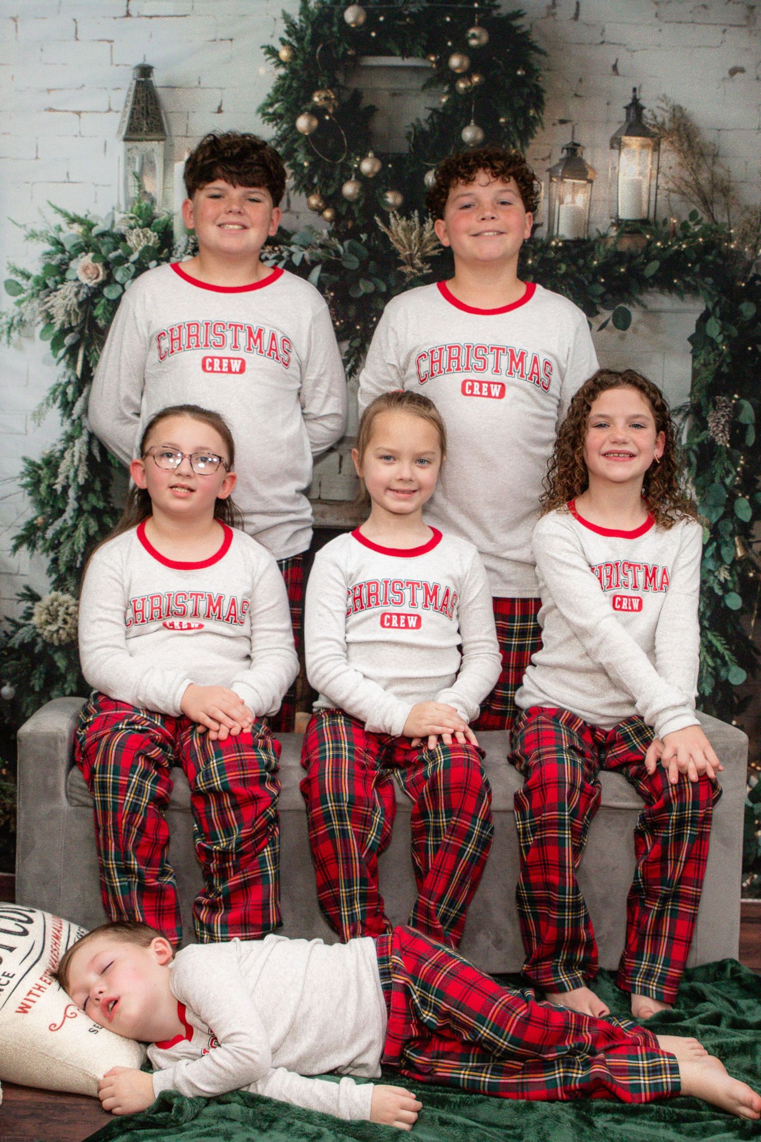 A group wearing matching Christmas-themed pajamas with white tops and red plaid pants pose against a holiday decorated backdrop.