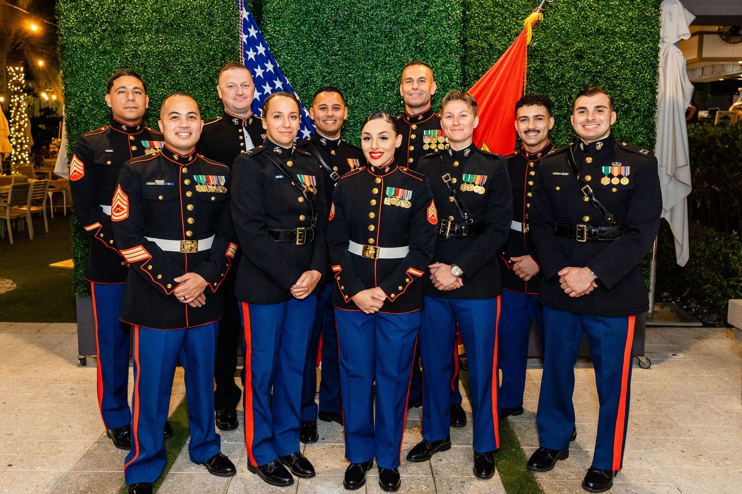 Military service members in dress uniforms pose together with flags and medals during a formal gathering event.