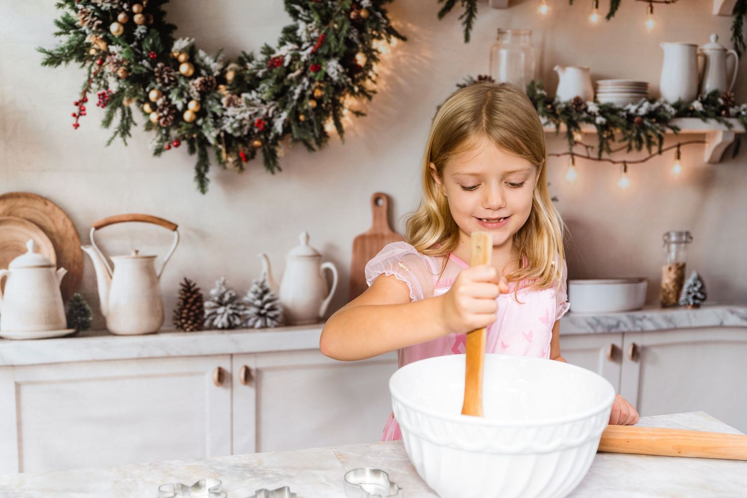 A festive holiday scene shows someone decorating cookies with icing while evergreen garland adorns the background.