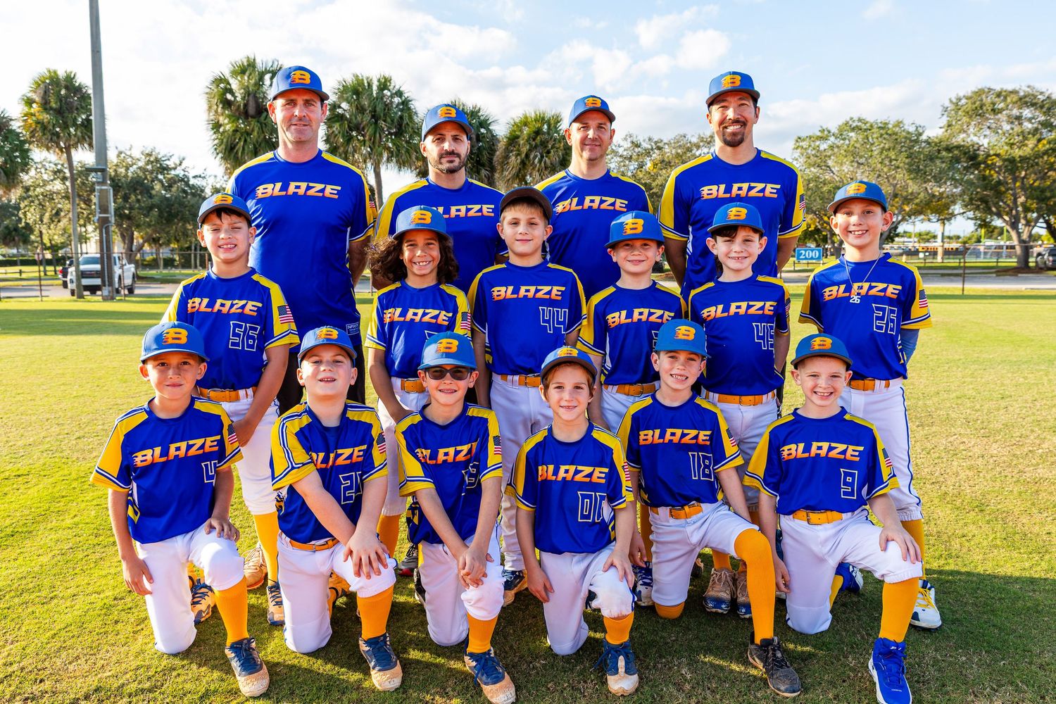 Youth baseball team wearing blue jerseys poses together on sunny field during sports season.