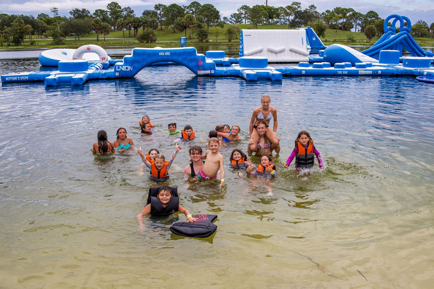 People enjoying an inflatable water obstacle course at a beach or water park with blue floating platforms.