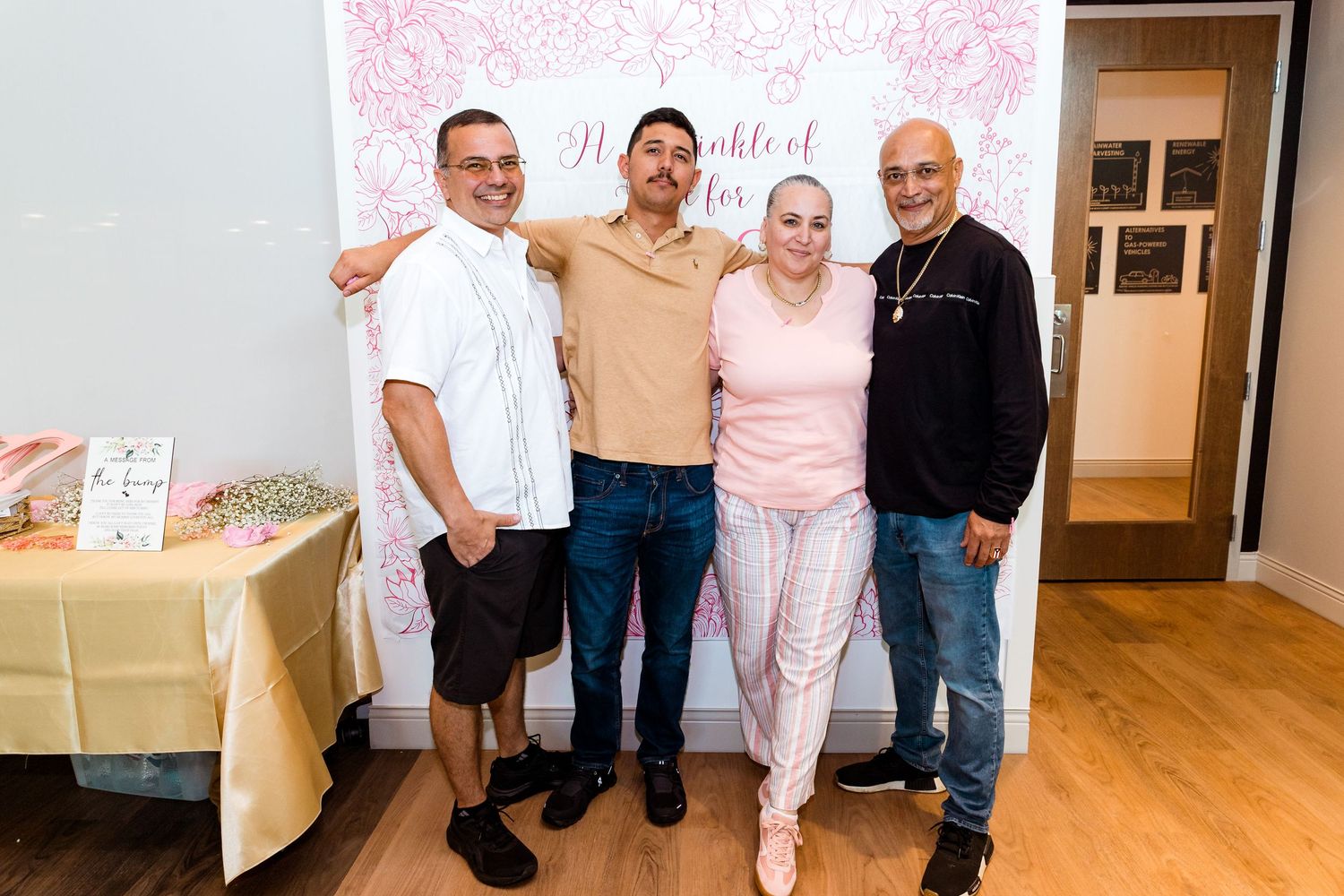 People posing together against a pink floral backdrop at an indoor event.