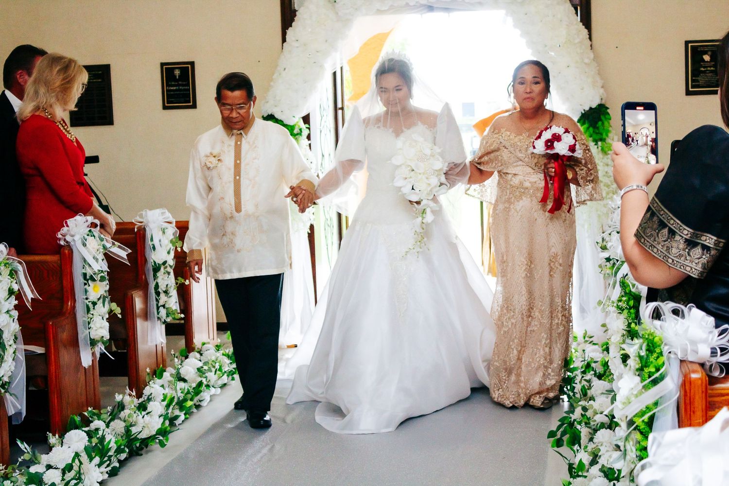 Wedding ceremony procession in a church aisle decorated with white floral garlands.