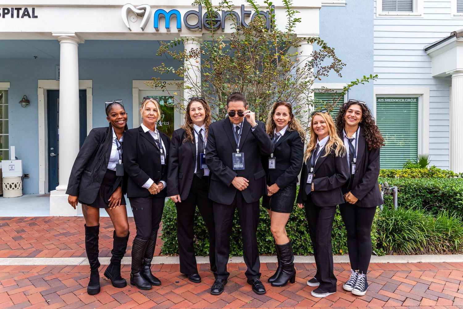 A group of students wearing matching dark uniforms pose together outside a building entrance.