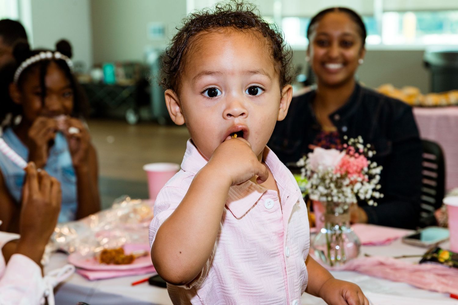 A baby in pink attire at what appears to be a celebration.