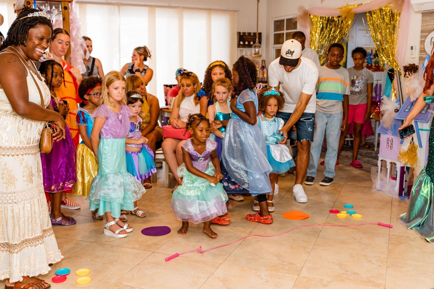 Children participate in an active indoor dance or movement class with colorful props and outfits in a bright studio space.