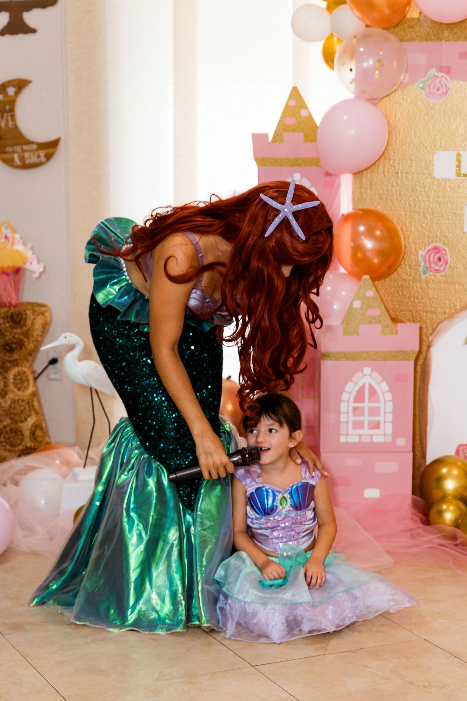 A magical princess party scene with sparkly dresses against a pink castle backdrop with balloons.