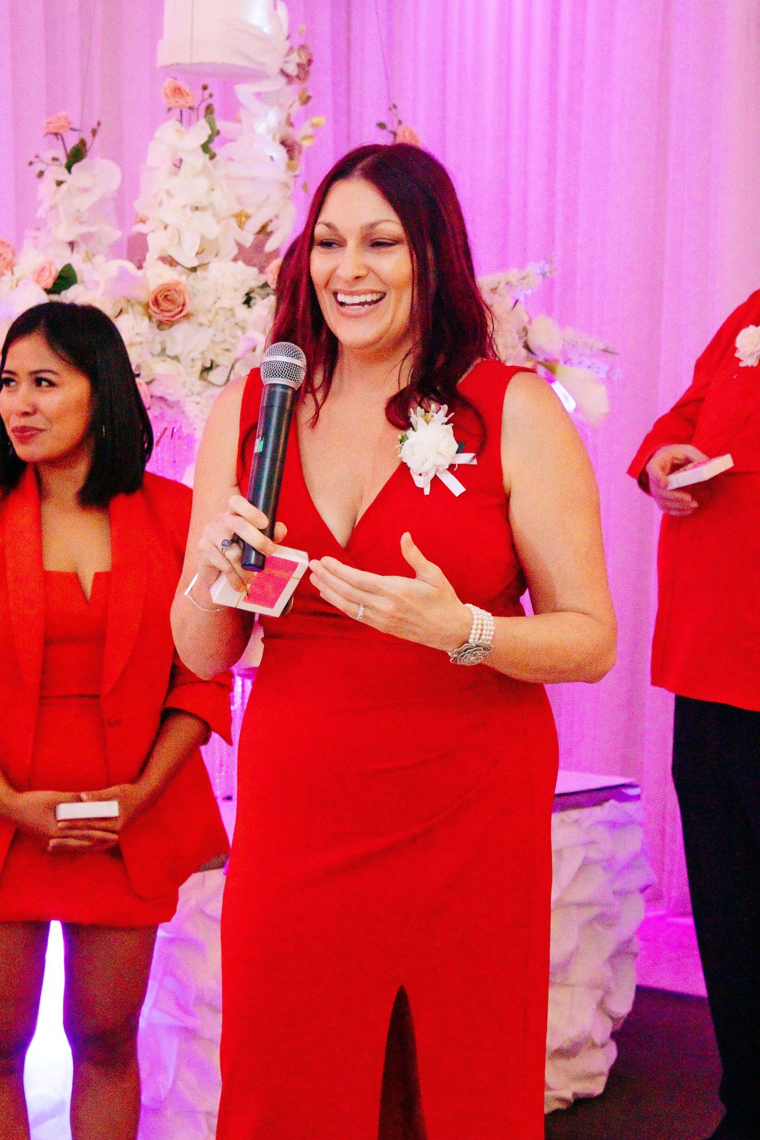Bridesmaids in matching red dresses at a wedding reception with pink backdrop.