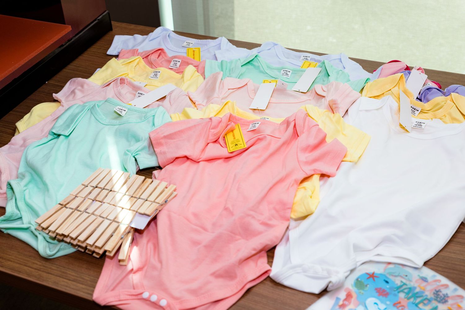Collection of pastel colored baby onesies and clothing items displayed on a table.