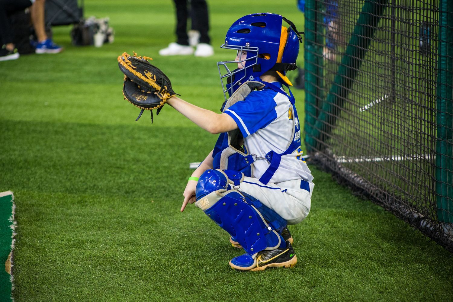 Baseball catcher in blue and white uniform crouching in ready position.