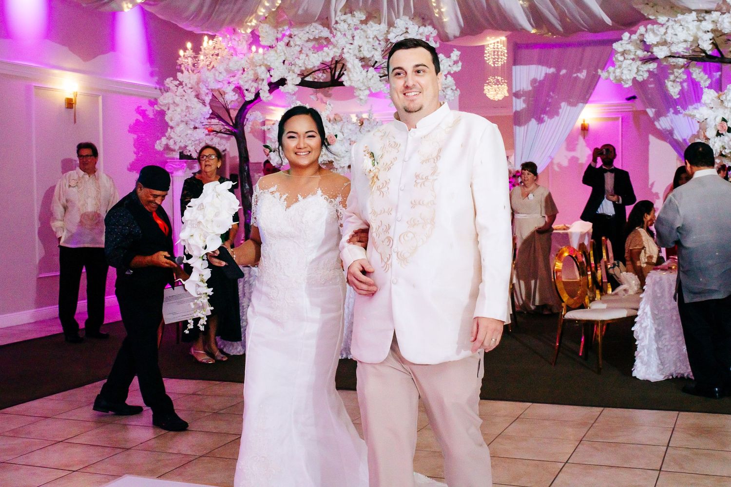 Bride and groom stand together at their wedding reception in elegant white formal wear.