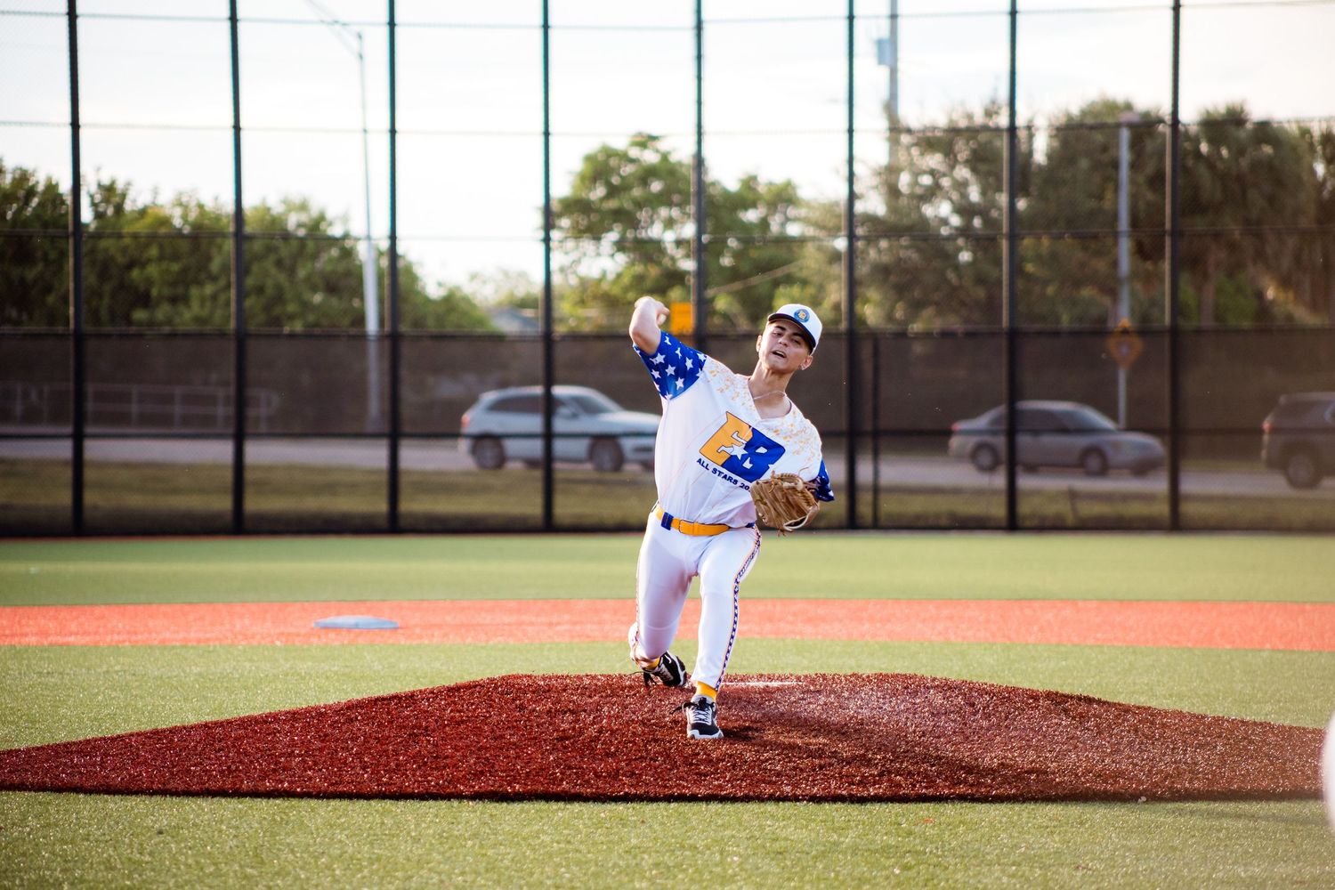 Baseball pitcher in blue and white uniform throws from red dirt pitching mound during game at outdoor field.