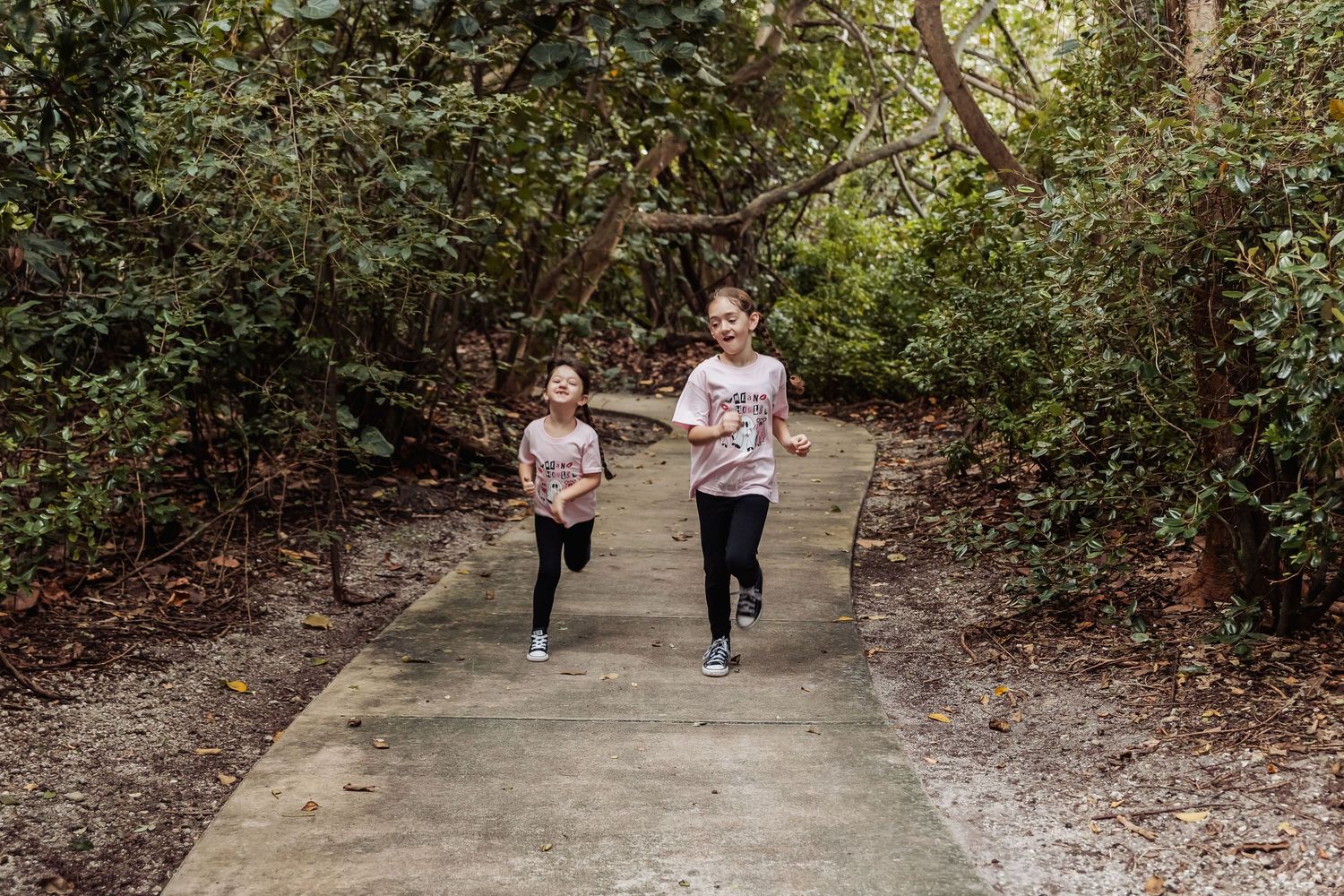 People walking together on a shaded dirt path through a wooded area on a sunny day.