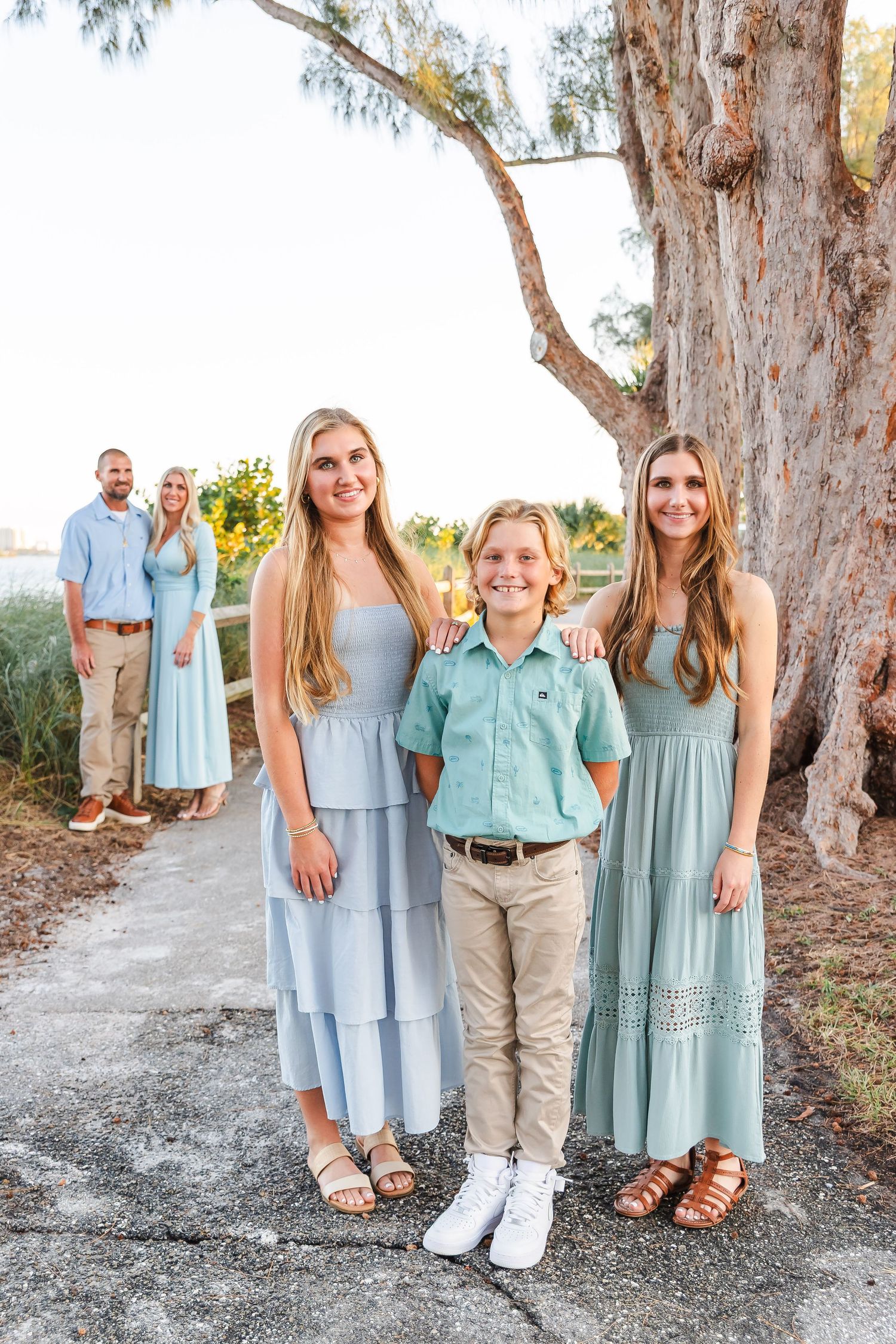 Casual family portrait session with everyone dressed in coordinating shades of blue and mint against trees.