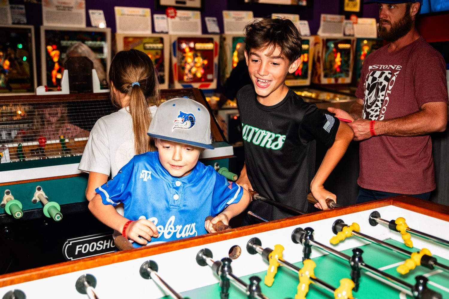 Two young boys playing a foosball game in an arcade or entertainment venue.