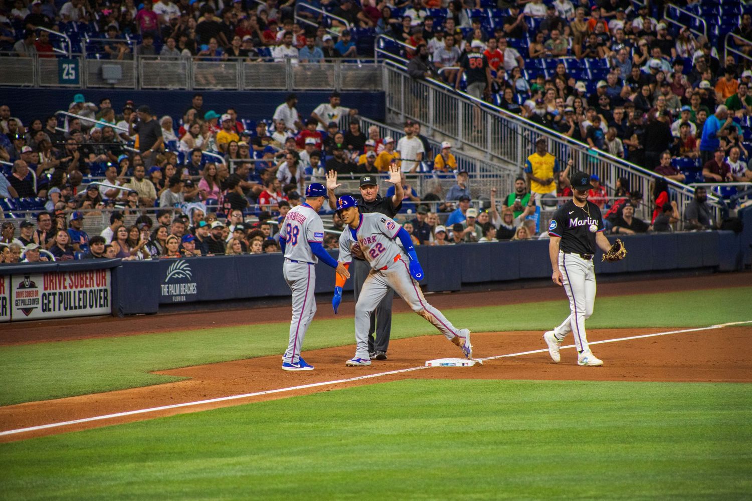Baseball players gather around first base during professional game with crowd in background.