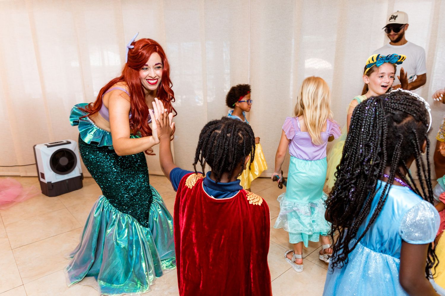 Kids dressed in colorful costumes dance with a mermaid performer at a fantasy costume party.
