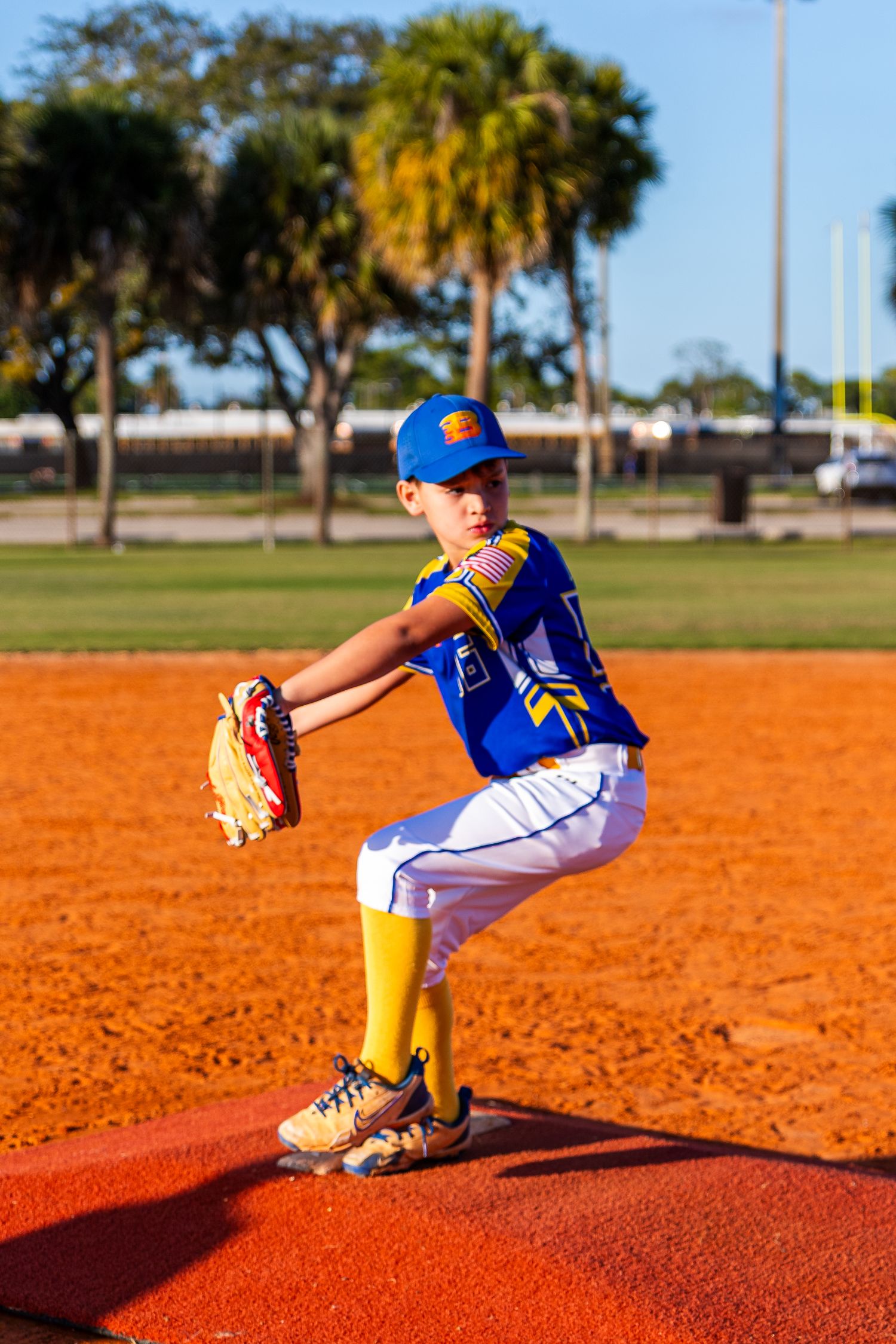 Baseball pitcher in bright blue jersey shows follow-through mechanics on pitching mound at outdoor field.