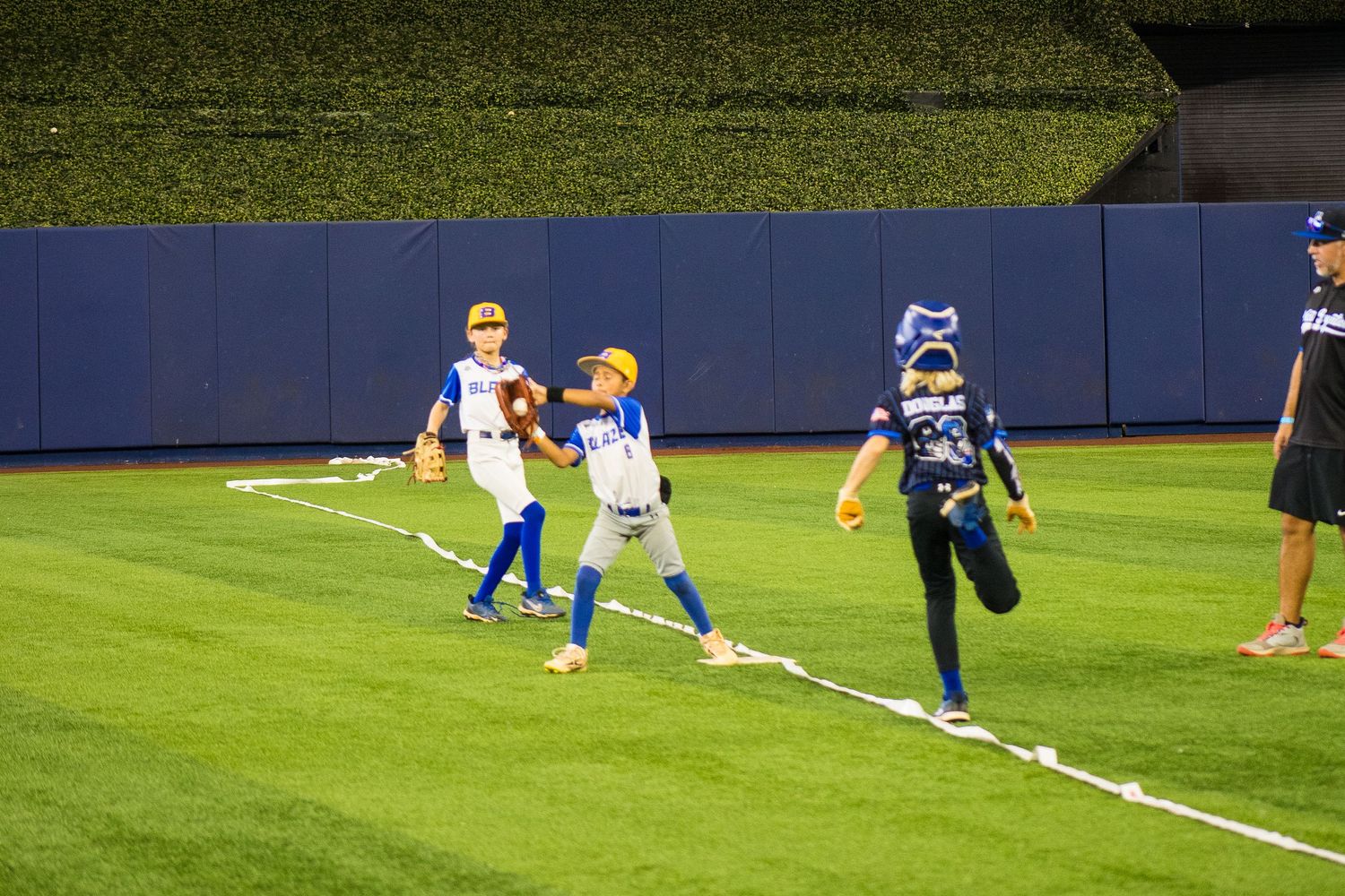Players practicing baseball drills on a green outfield at night with blue stadium walls in the background.