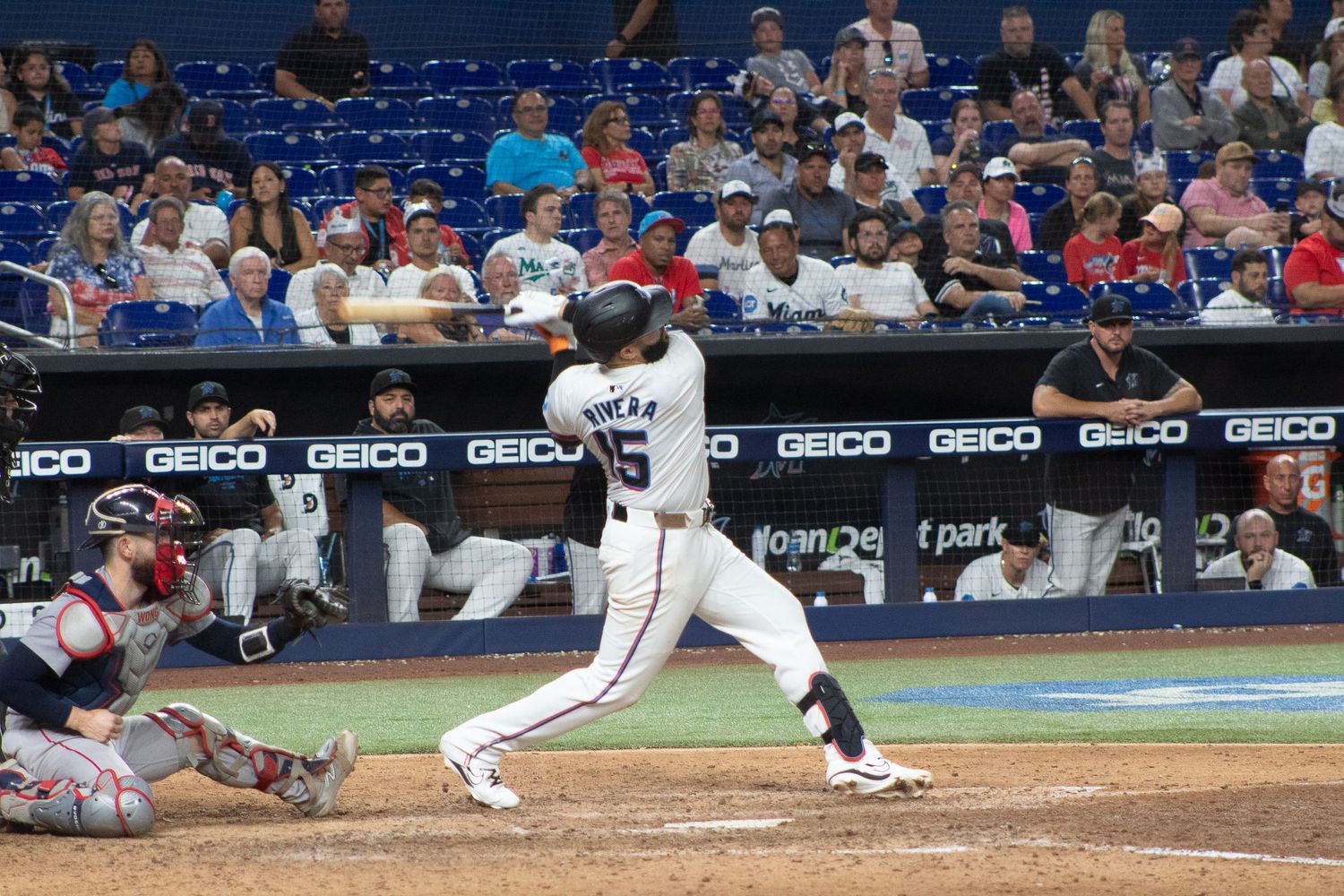 Baseball batter swings at pitch during game with crowd in background.