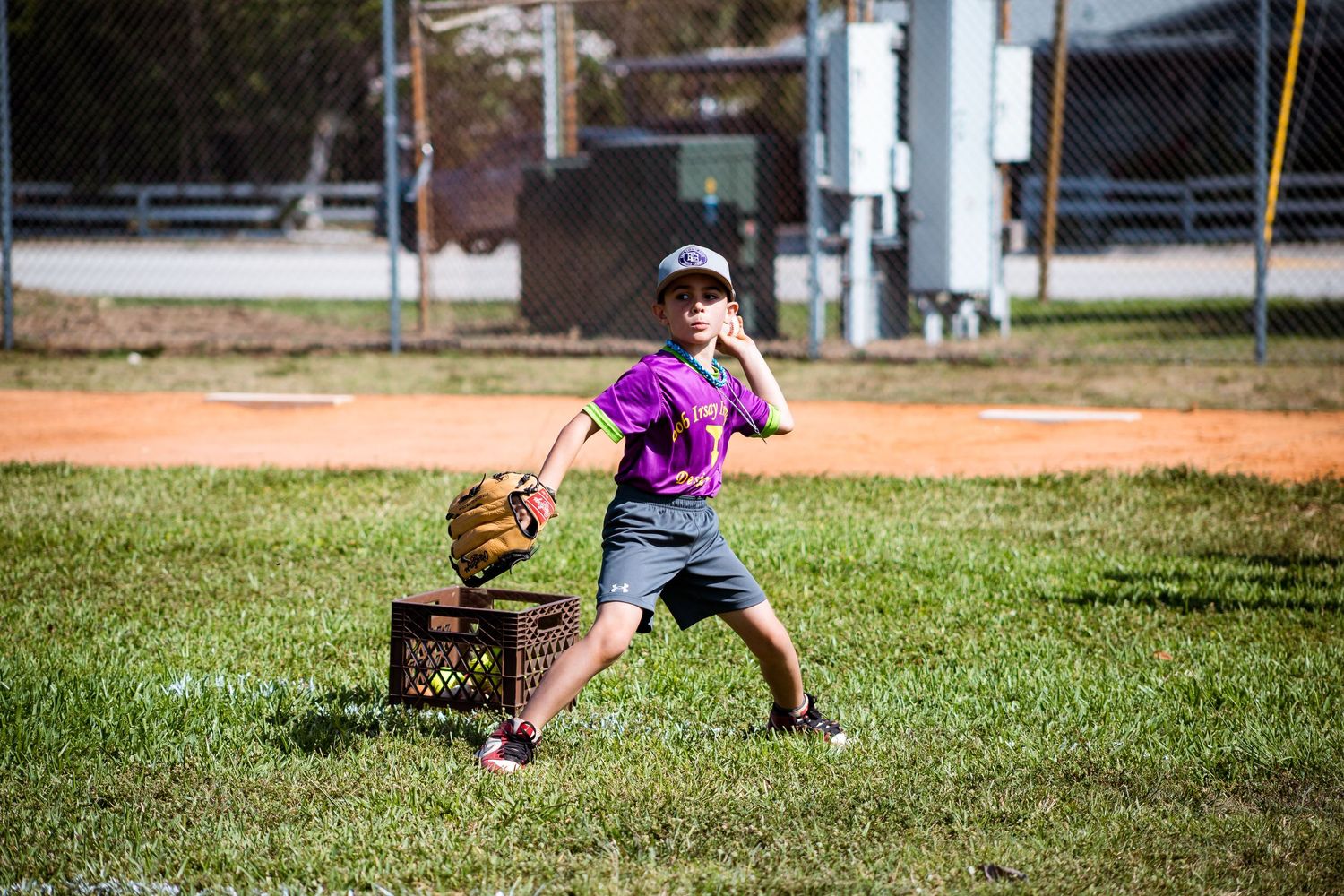 Young baseball player in purple shirt practices throwing techniques on a field.