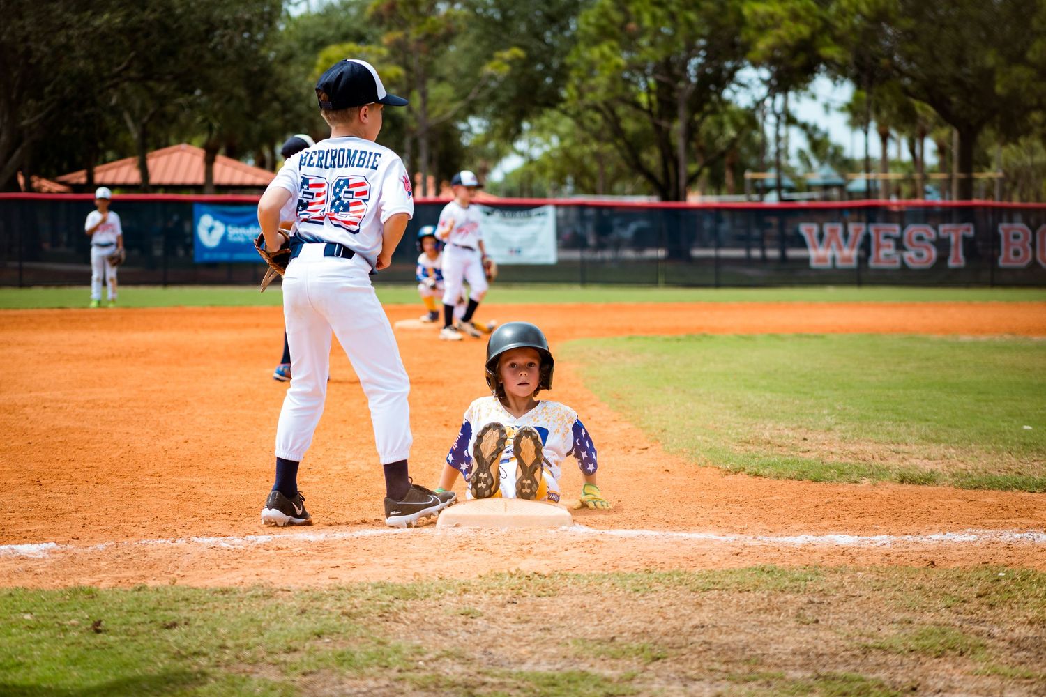 Baseball player in white uniform at bat while catcher crouches behind home plate during game on dirt field.