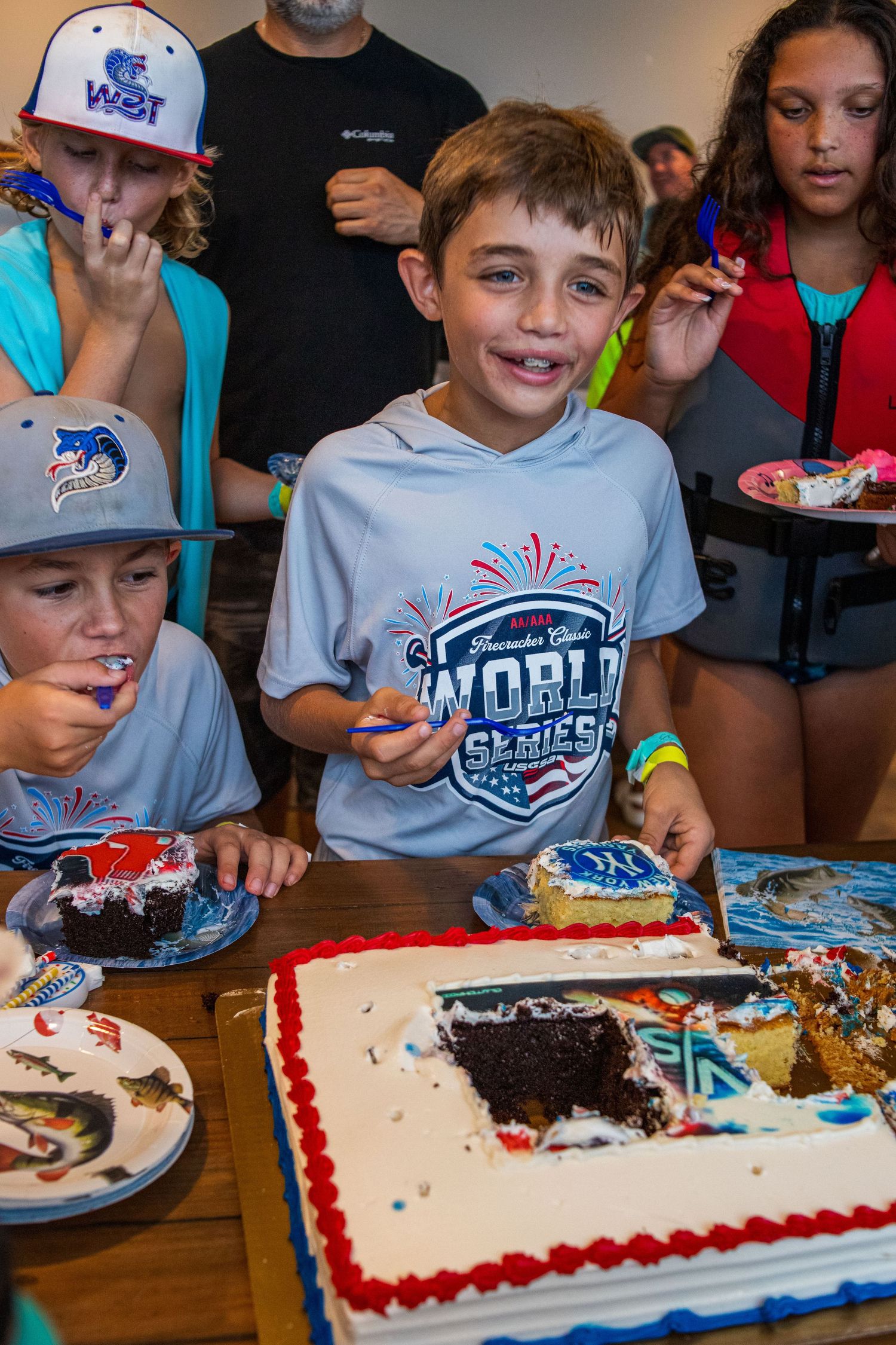Group gathered around birthday cakes with red and blue frosting at what appears to be a sports-themed celebration event.