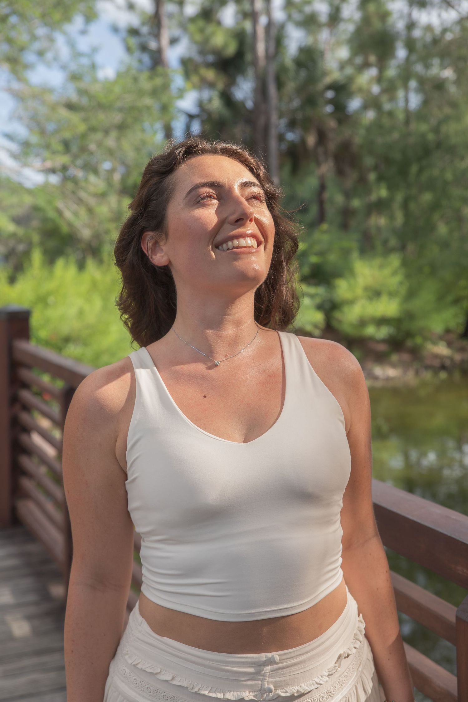 Person in white top smiling joyfully while enjoying nature outdoors.