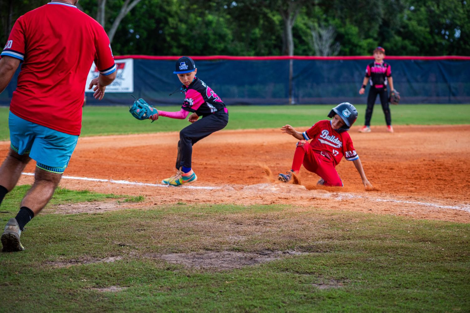 Baseball players in red uniforms positioned on the field during a youth league game.