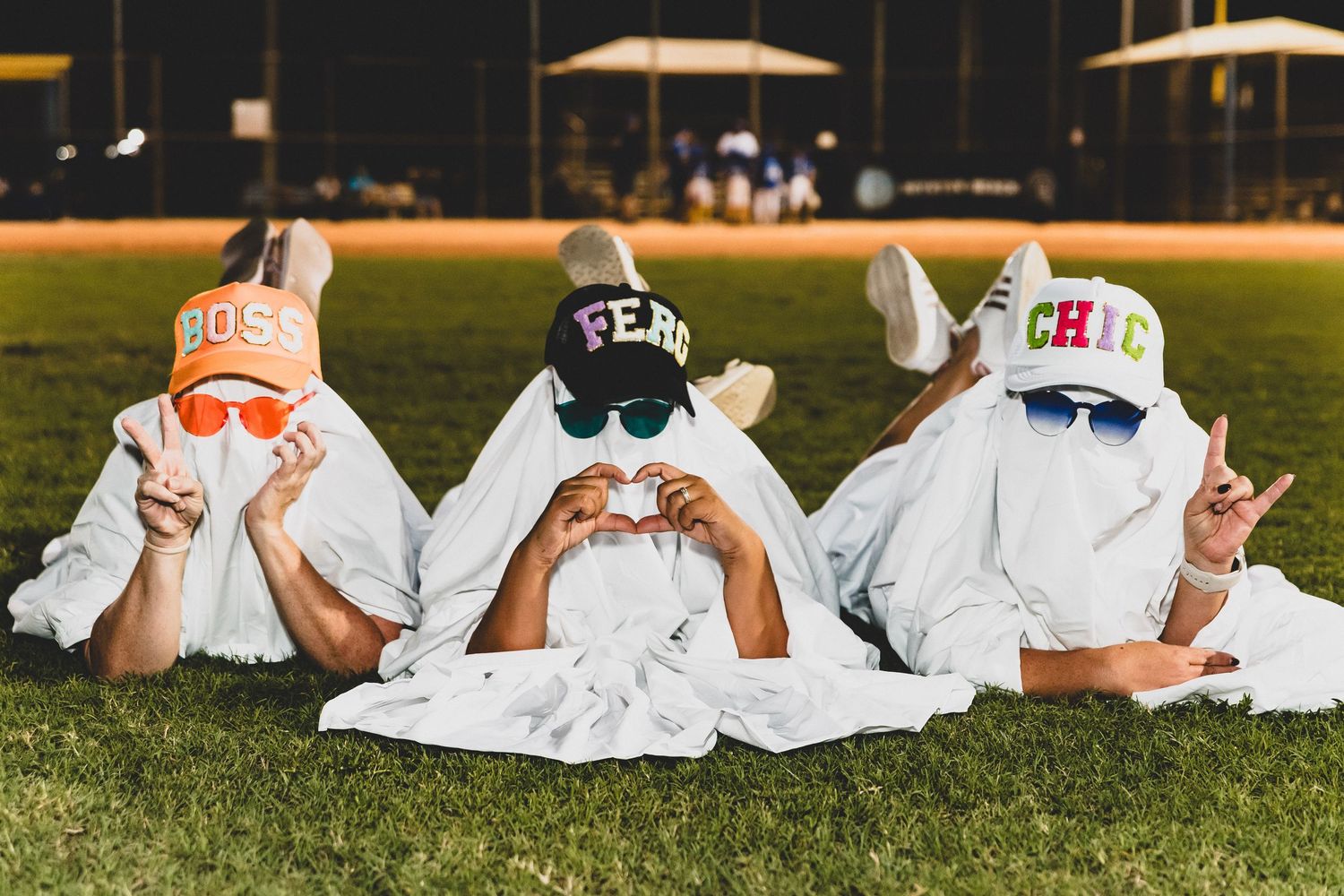 Group in white ghost costumes lay on grass field during nighttime event.