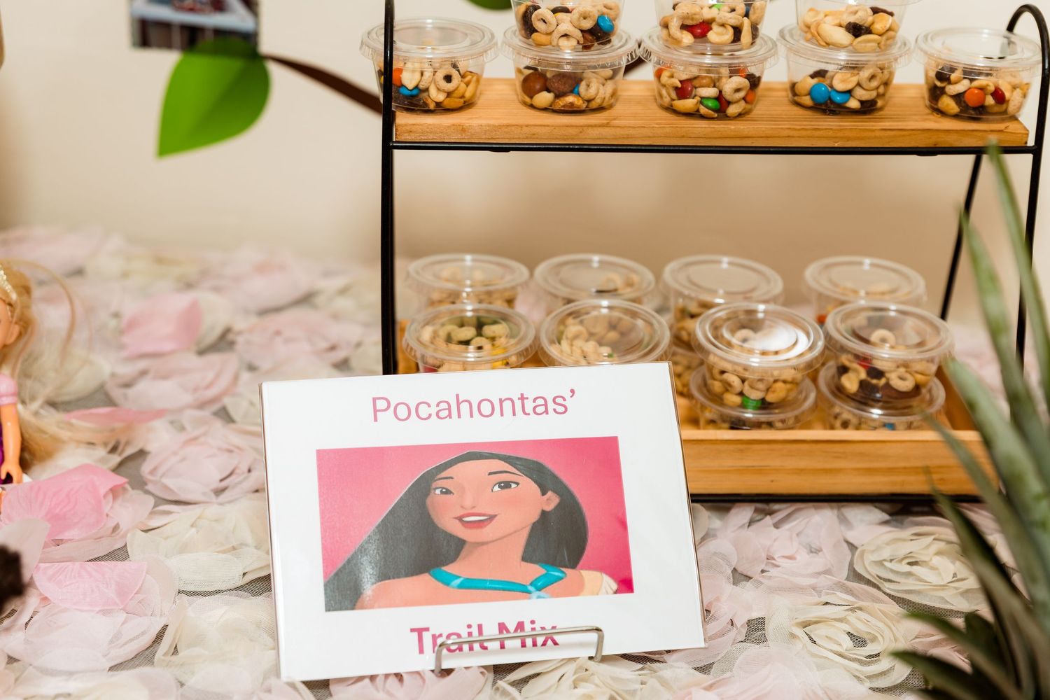 A themed trail mix station with character signage displayed on a floral tablecloth.