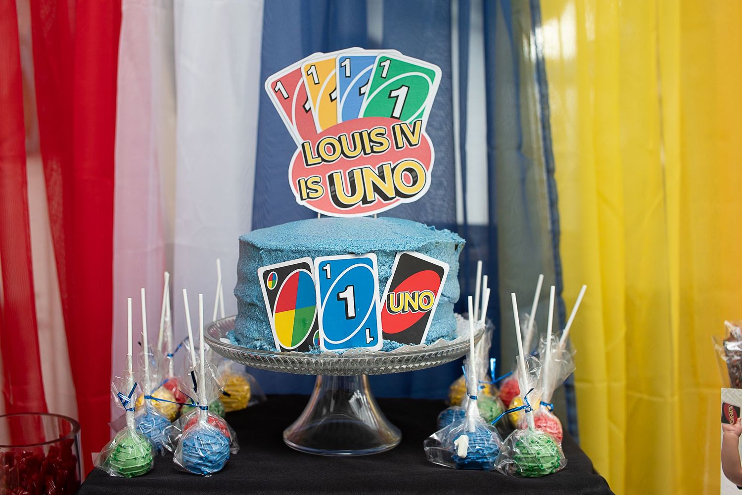 A themed birthday cake featuring UNO card game design with colorful decorations and lollipop party favors on display.