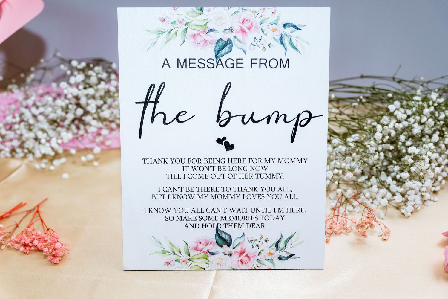 A baby shower card with floral design reads 'A Message from the bump' on a table with pink decorations.