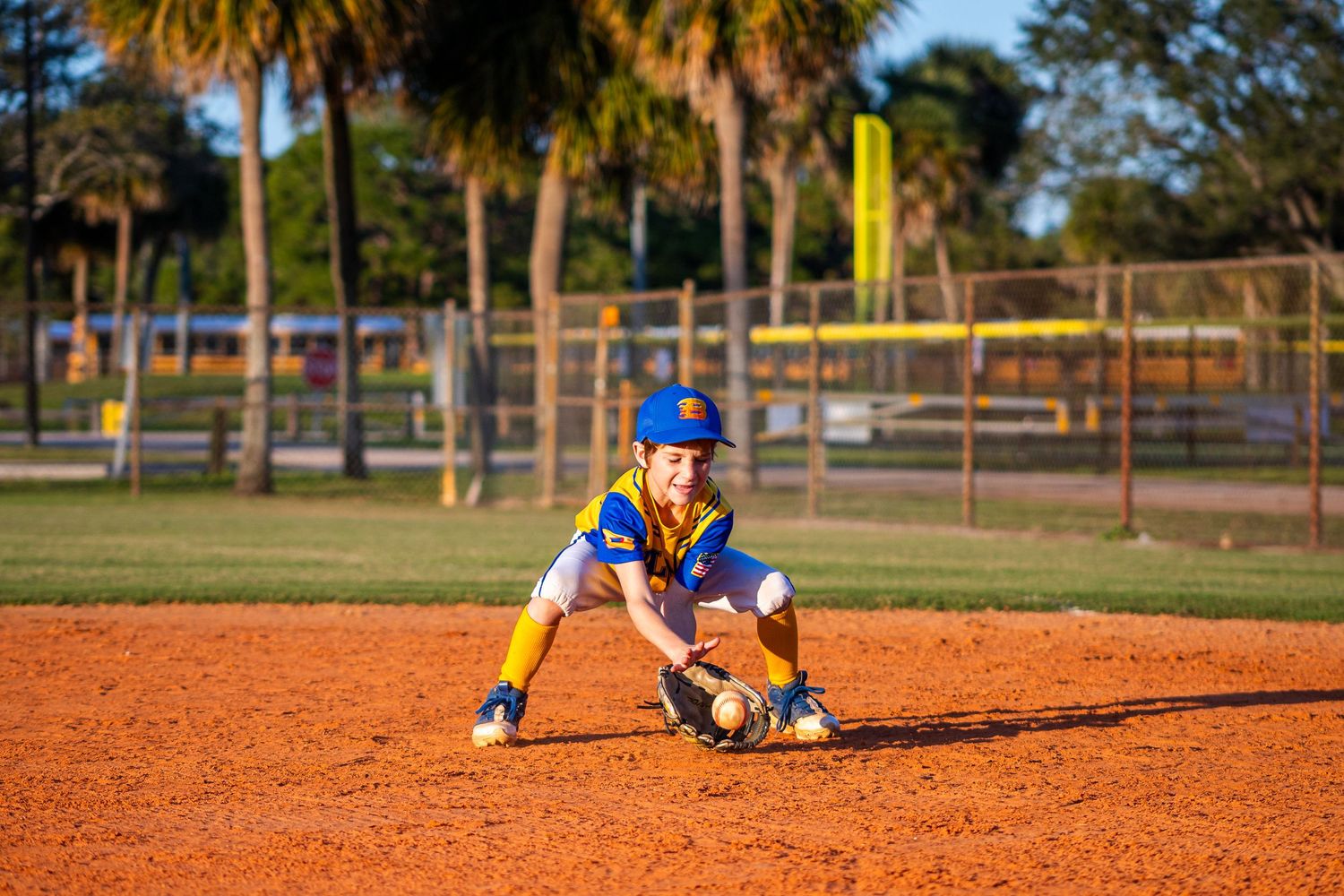 Baseball player fielding ground ball on orange clay infield during practice or game.