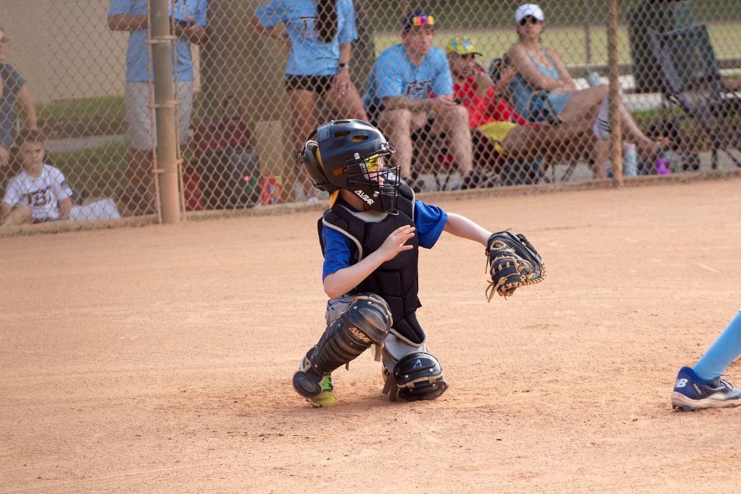 Youth baseball catcher in protective gear crouching behind home plate.